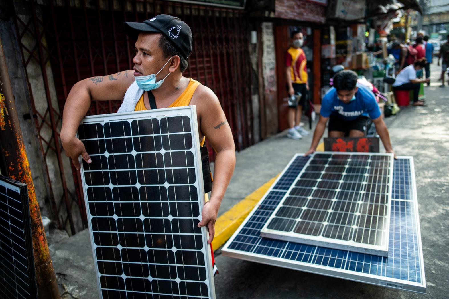 <p>homens carregam painéis solares</p>
