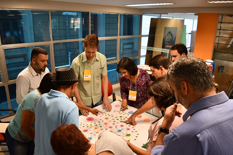 <p>imagem mostra participantes de oficina ao redor de uma mesa trabalhando no planejamento</p>